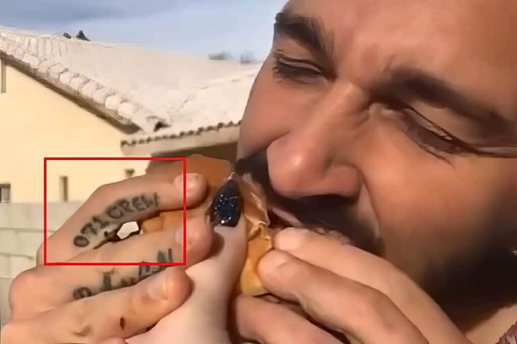 Close-up of a young man eating a burger outdoors, showing tattoos on his fingers and a focused expression. The image emphasizes masculinity and personal style, fitting for men’s lifestyle content.