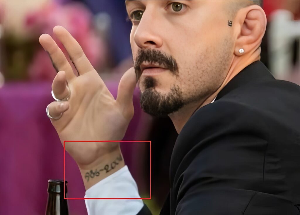 Close-up of a stylish man with a beard, mustache, and tattoos, wearing earrings, looking serious in a social setting. Captures men's fashion, grooming, and tattoo trends relevant for men's lifestyle content.