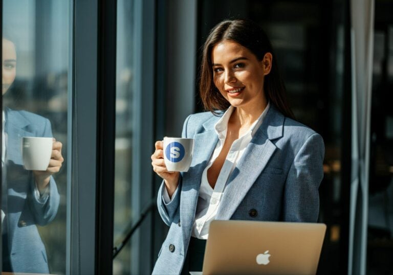 Professional businesswoman with coffee mug in modern office setting, dressed in smart blazer, with Apple MacBook, representing business, success, and workplace lifestyle.
