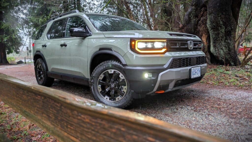 An eye-catching Honda SUV driving through a damp woodland environment with lush green trees and a muddy path, showcasing rugged off-road capability for outdoor exploration enthusiasts.