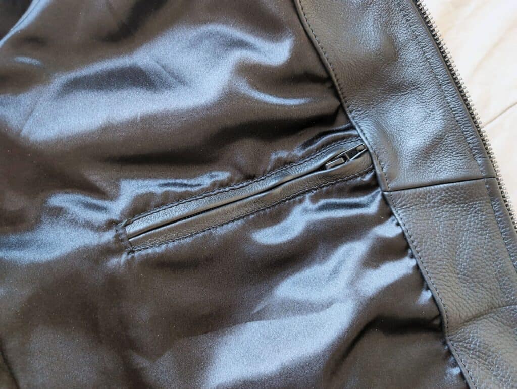 Close-up view of a black leather jacket interior featuring a zipper pocket and shiny satin lining, highlighting men's fashion accessories and clothing details.