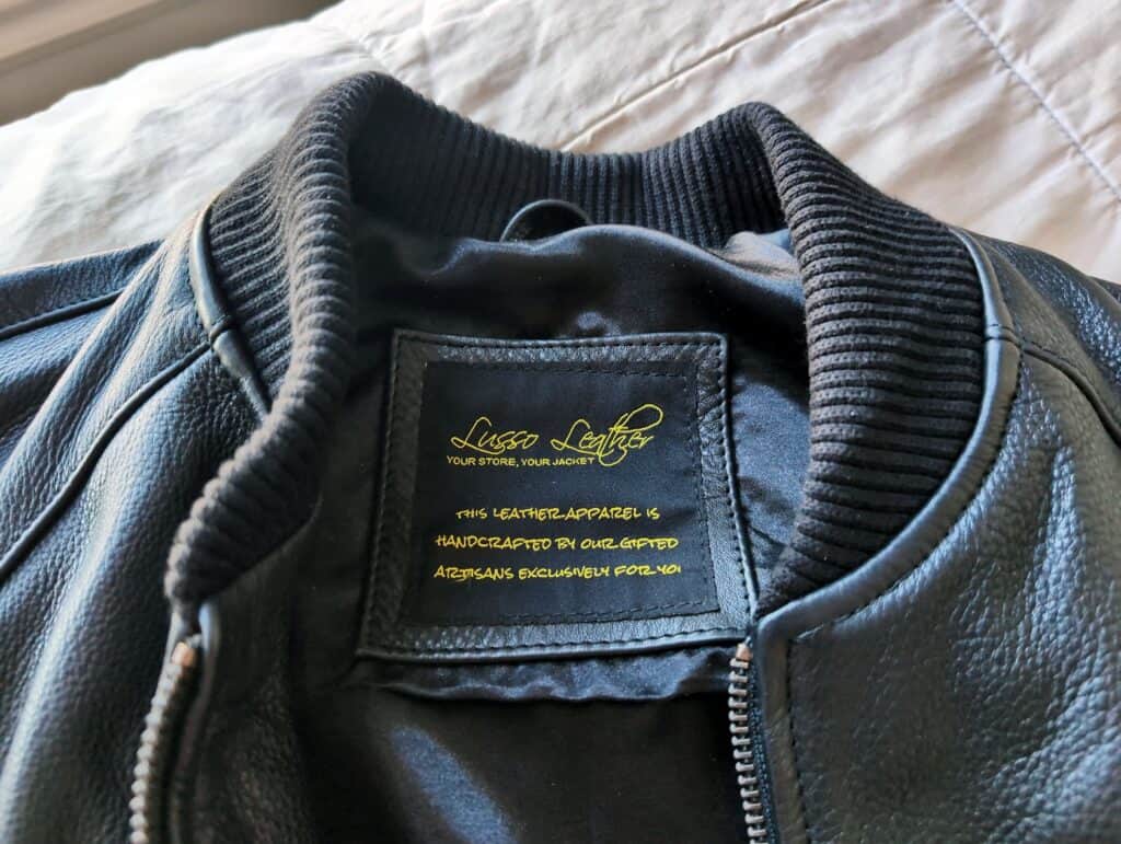 Close-up of a stylish black leather bomber jacket featuring a ribbed collar, zipper accents, and a label from Lusso Leather indicating handcrafted quality and exclusive craftsmanship.