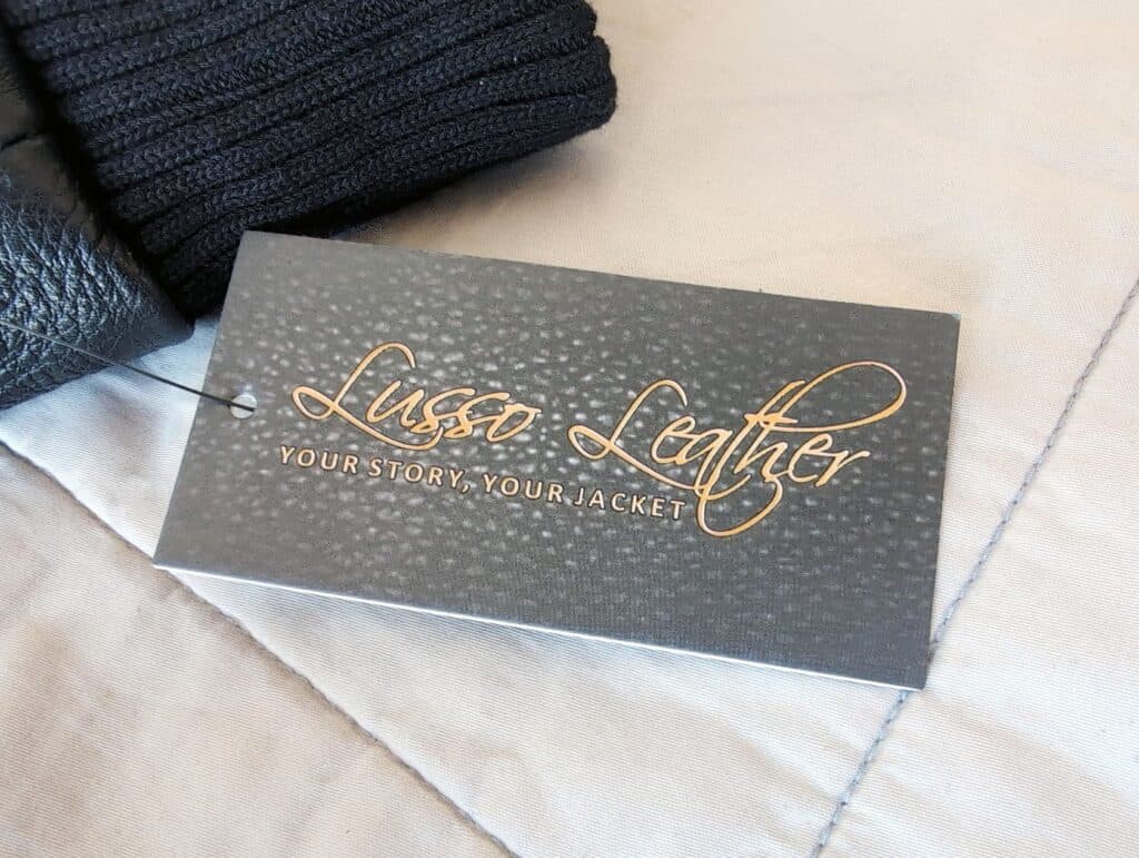Photo of a stylish black label from Lussor Lather, featuring the tagline "Your Story, Your Jacket," on a sophisticated fabric background.