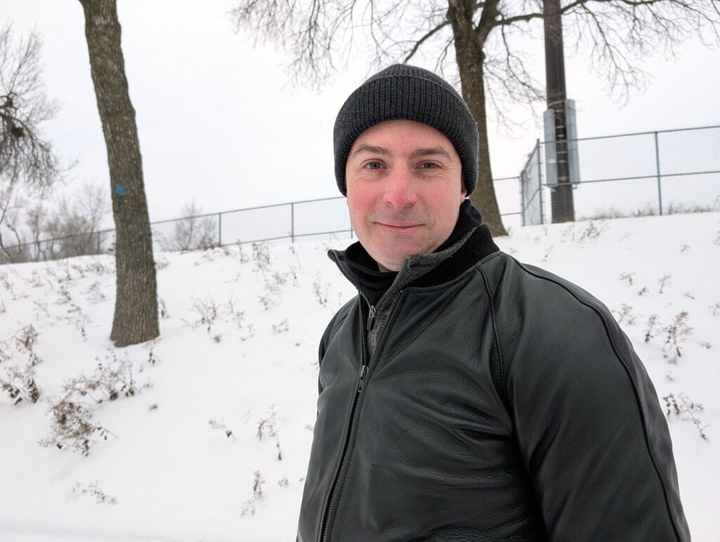 Lusso Leather Black Bomber Style Ribbed Jacket Review 6 Close-up of a man wearing a black beanie and leather jacket standing in snowy park during winter.