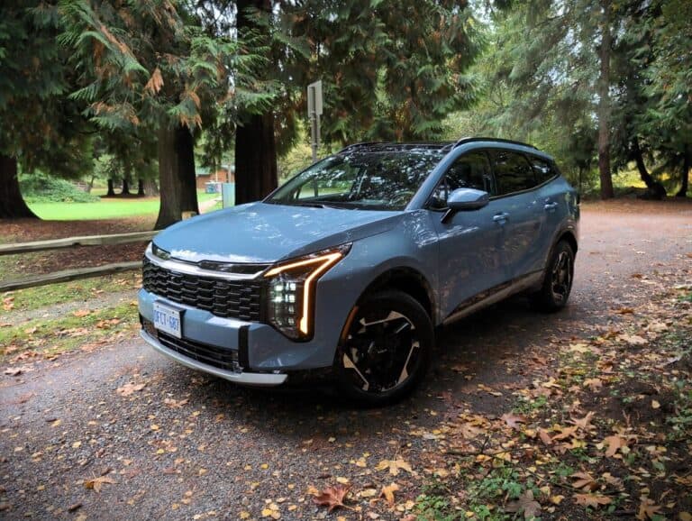 New 2026 Kia Sportage EX Hybrid parked outdoors among trees, showcasing its modern design and eco-friendly hybrid technology.