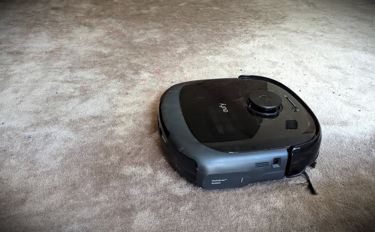 Eufy Omni E28 robot vacuum cleaning a beige carpet, featuring a sleek black design with a top-mounted control dial, ideal for smart home cleaning solutions.