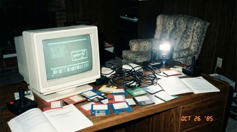 Vintage computer workstation with CRT monitor, floppy disks, and scattered documents, reflecting technology and office environment from the 1980s.