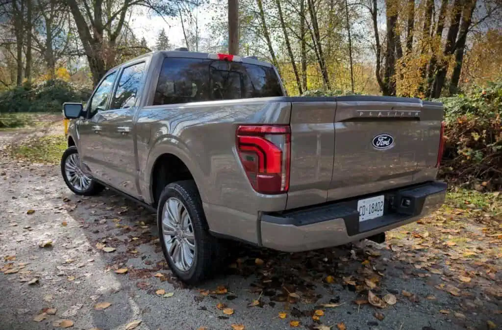 Enhanced view of the 2026 Ford F150 SuperCrew Platinum Hybrid pickup truck parked outdoors in a wooded area, showcasing its modern design and premium features.