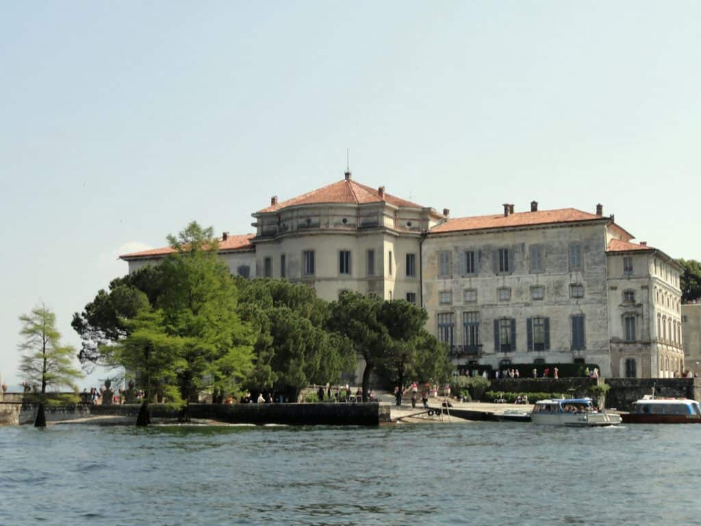 Scenic view of a historic Italian garden with lush trees and a grand lakeside villa, showcasing Italy's beautiful landscape and architecture.
