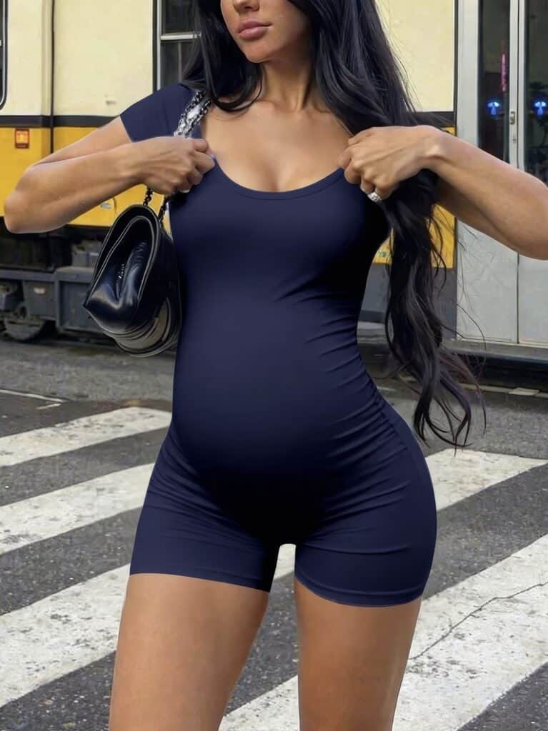 Pregnant woman in navy blue athletic outfit, highlighting her baby bump, standing outdoors on a city street, emphasizing confidence and comfort during pregnancy.