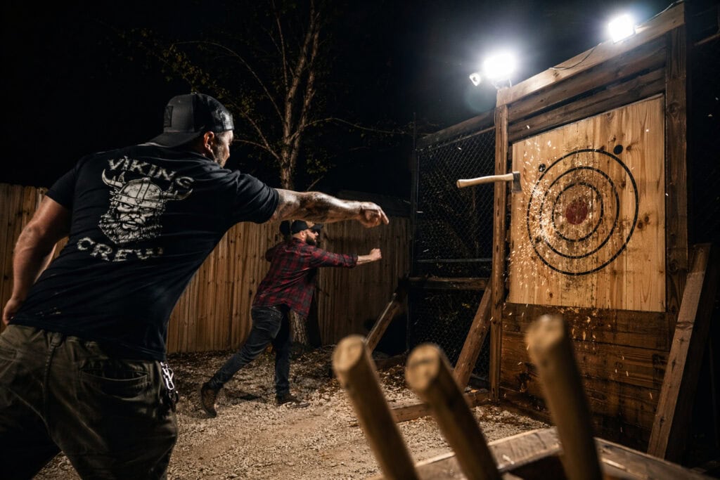 Man throwing axe at outdoor target during nighttime.