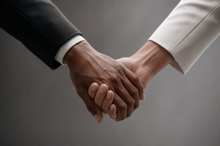 Handshake agreement between two business professionals, one in a black suit and the other in a white suit, symbolizing trust, partnership, and collaboration in a professional setting.