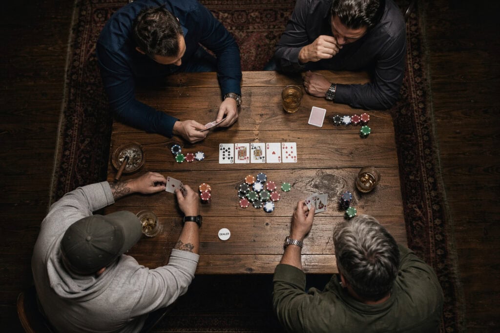 Four friends playing poker around a wooden table, enjoying a game night with chips, cards, and drinks, capturing a social and entertaining moment.