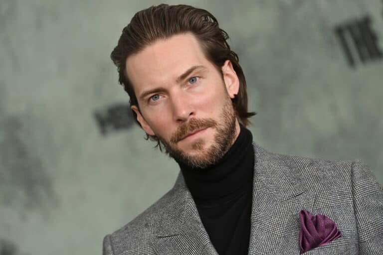 Troy Baker, actor and voice talent, dressed in a gray blazer and black turtleneck, attending a public event.