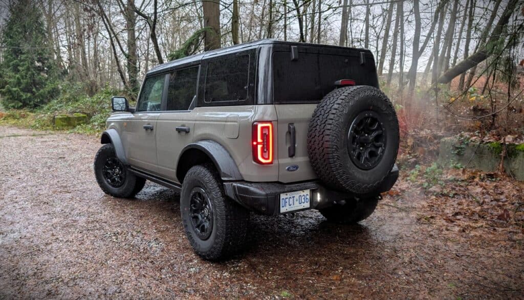2026 Ford Bronco Badlands 4-Door off-road SUV parked on a muddy trail in a wooded area, showcasing rugged design and outdoor adventure capabilities.