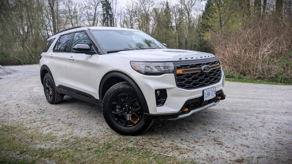 A detailed image of a white Ford Explorer SUV parked on a gravel path surrounded by trees and nature, showcasing modern automotive design and outdoor adventure readiness.