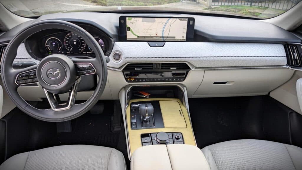 2026 Mazda CX-90 PHEV Signature Review 3 A sleek car interior featuring a modern dashboard with a digital display, steering wheel with controls, and a central console with gear shift and multimedia controls, emphasizing advanced automotive t.