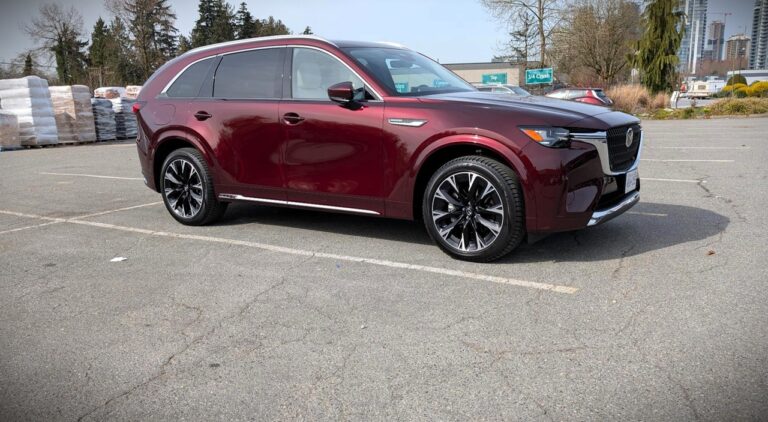 A sleek maroon Mazda SUV parked in an outdoor lot with cityscape and trees in the background, showcasing modern automotive design and style.