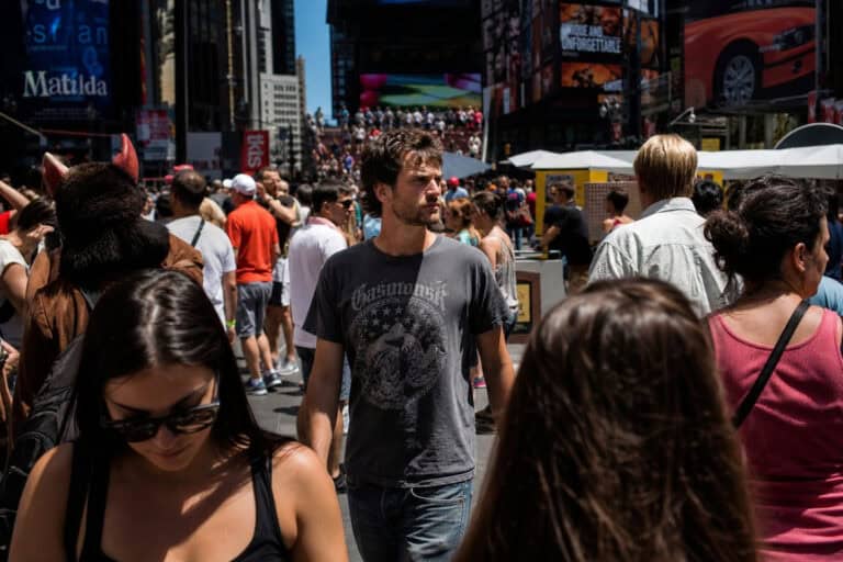 Crowded Times Square in New York City with diverse pedestrians, bright billboards, and vibrant urban atmosphere during daytime.