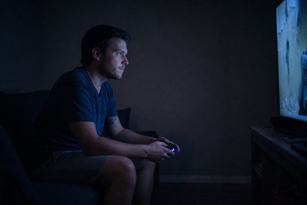 Stressed Out Man: Why Trying to 'Fix' Him Always Backfires 2 Young man playing video games on a console in a dimly lit room.