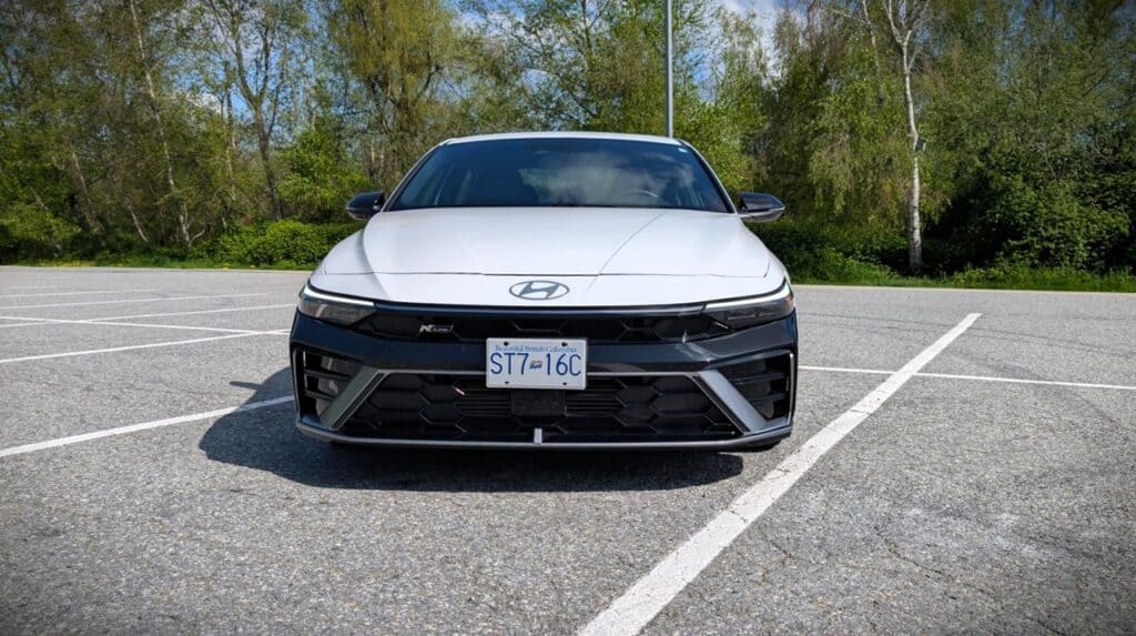 2026 Hyundai Elantra N-Line Review 2 Front view of a white 2026 Hyundai Elantra N-Line parked in an empty lot with trees in the background.
