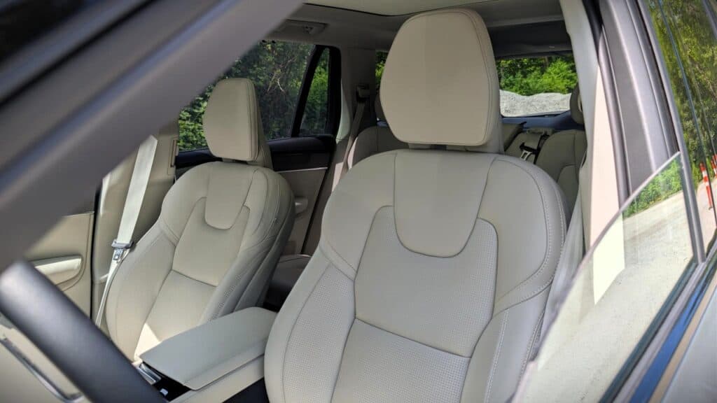 A lush, green outdoor scene visible through the windows of a modern, beige leather interior car seat.