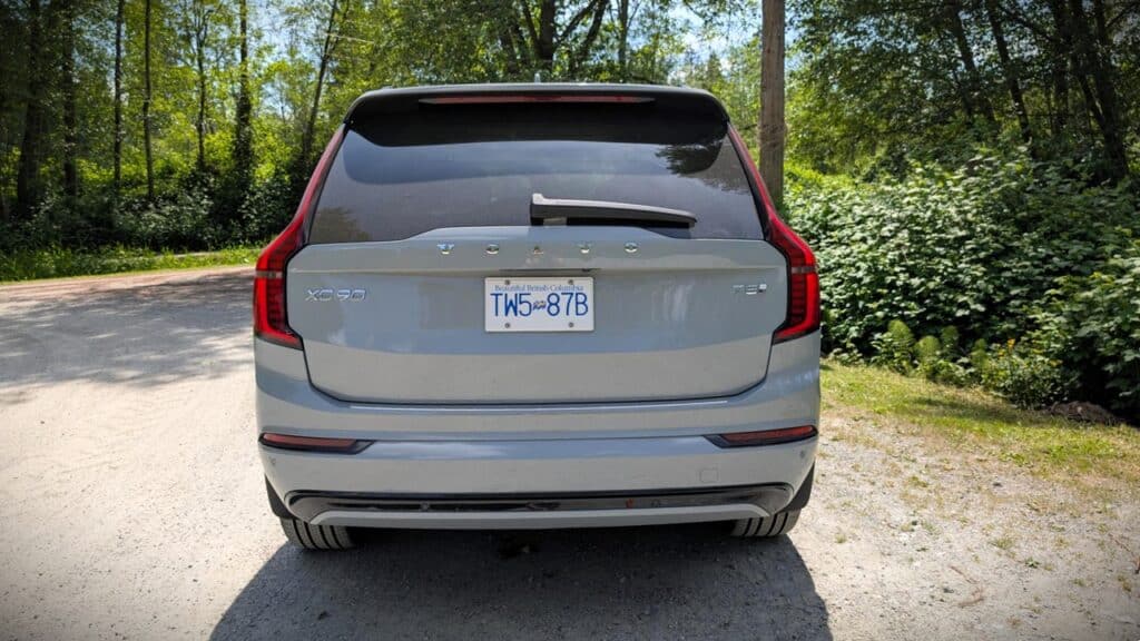 A detailed view of the rear of a modern silver SUV parked on a dirt road surrounded by lush green trees and foliage, showcasing the vehicle's sleek design and spaciousness in a natural setting.