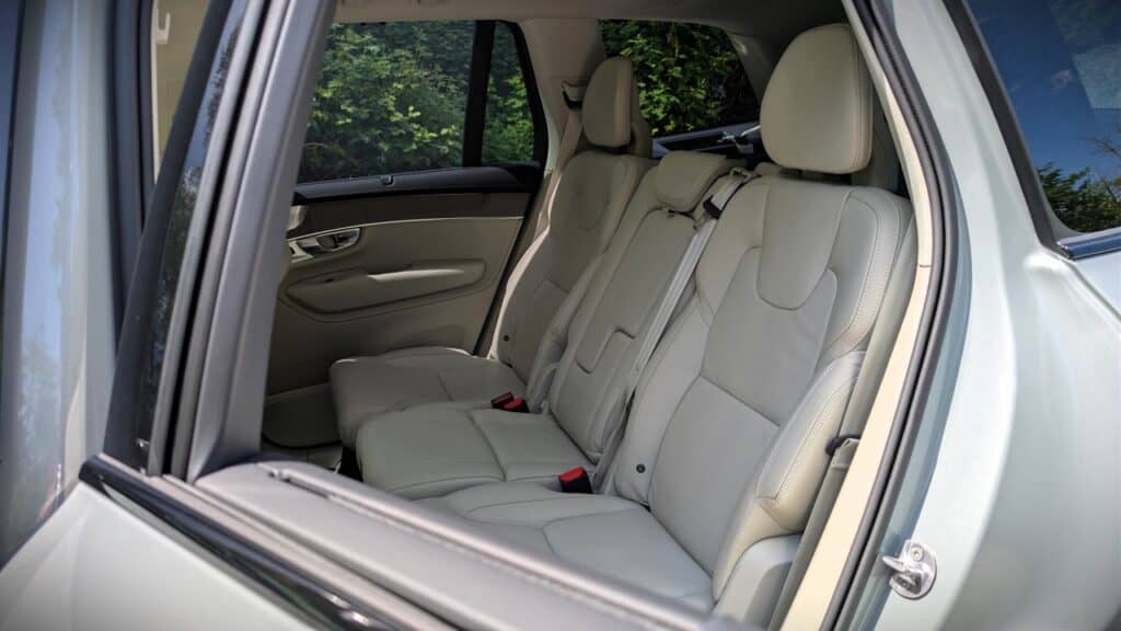 A comfortable beige leather car interior with three rear seats, headrests, and seat belts, viewed through the open rear window. Perfect for family trips and daily commuting.