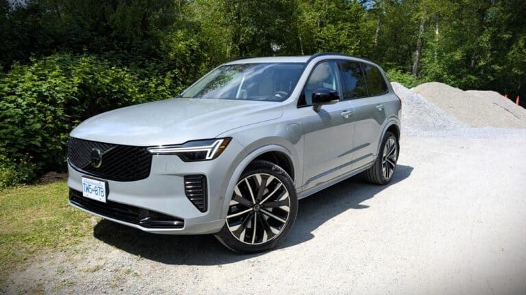 A detailed view of a modern silver SUV parked outdoors on a gravel surface, surrounded by lush green trees, showcasing contemporary automotive design and features.