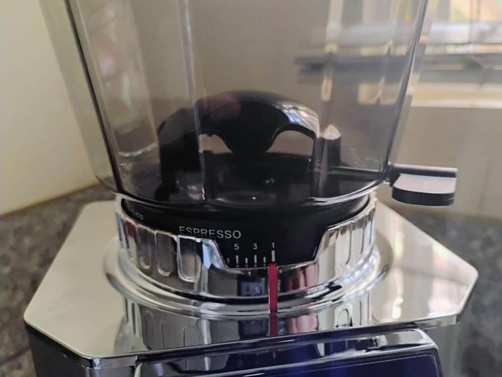 AMZCHEF Professional Coffee Grinder Review 2 Close-up of an espresso coffee grinder with a transparent bean hopper and a metallic base, set on a kitchen countertop.