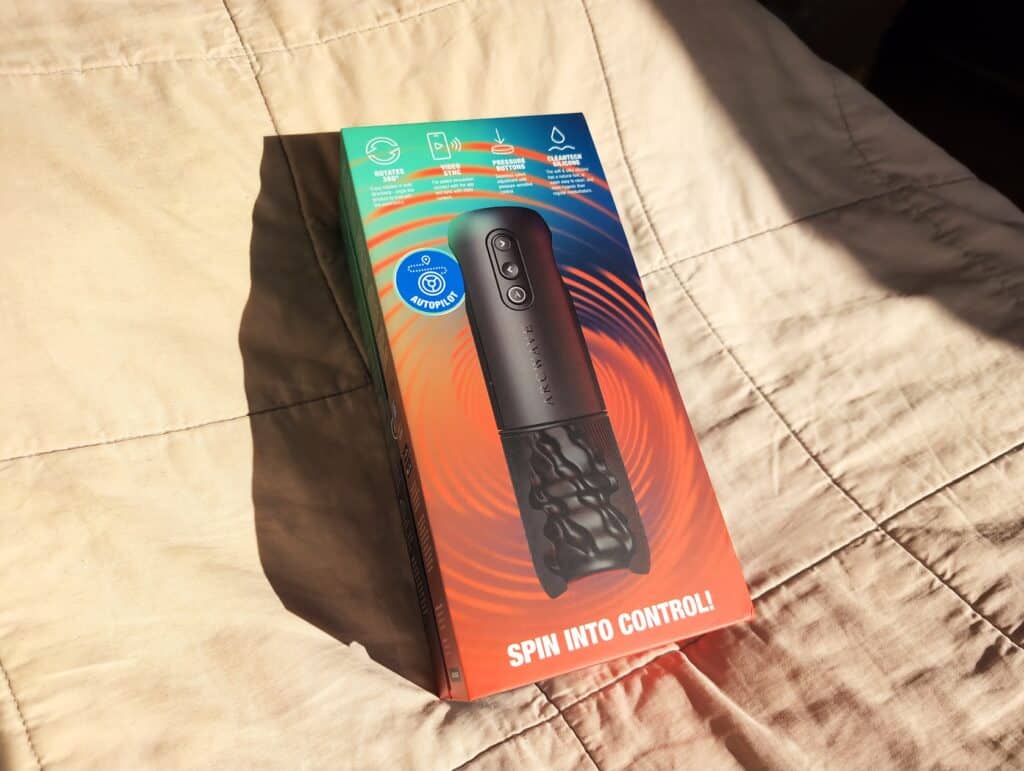 Unfinished Man review of Arcwave Orbit: compact, black rotating stroker with control buttons, in colorful packaging on a beige fabric surface.