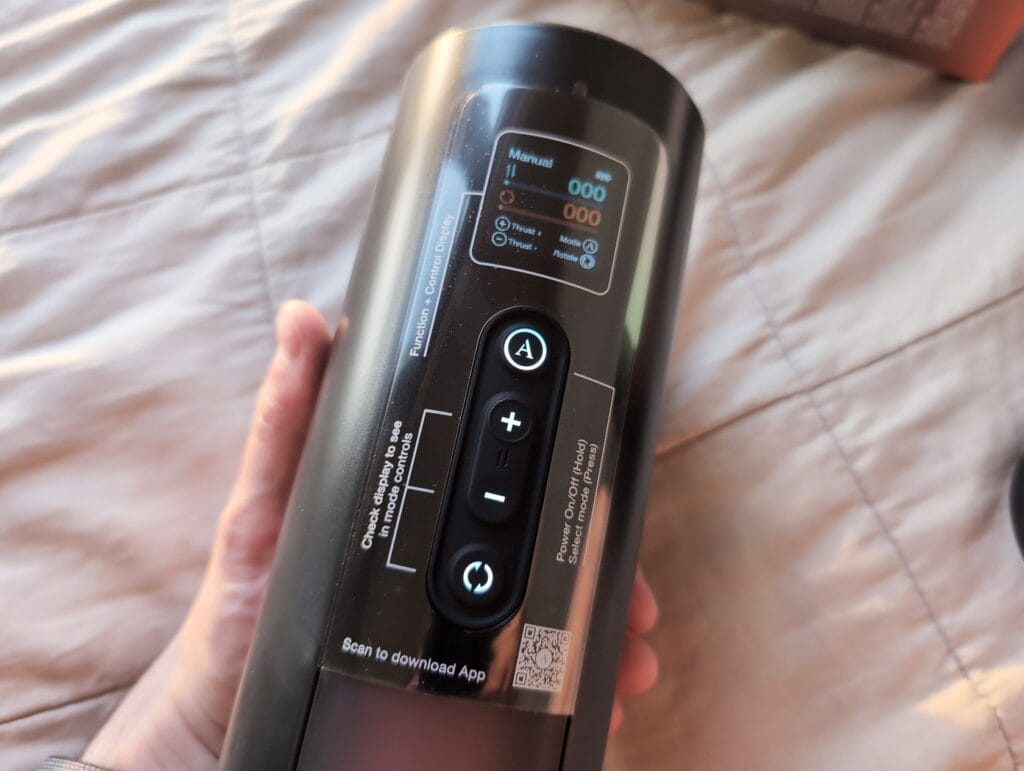 Close-up of a black cylindrical device with digital display and control buttons, held in a person's hand on a bed.