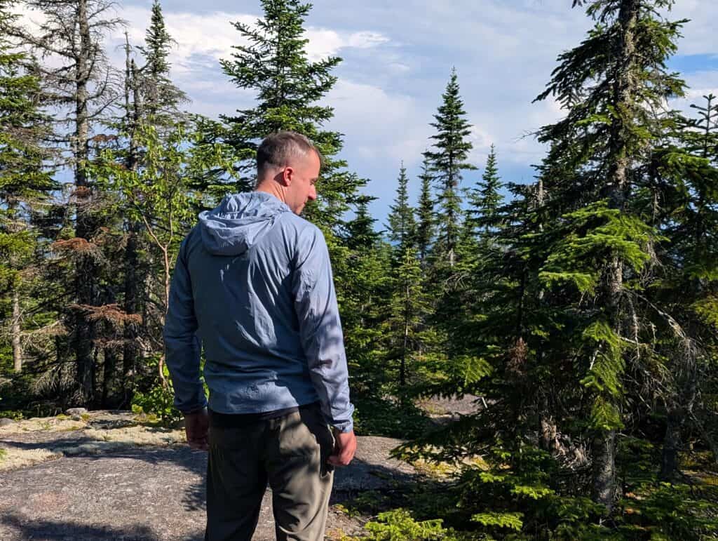 Man hiking in a forested area with tall pine trees and a partly cloudy sky.