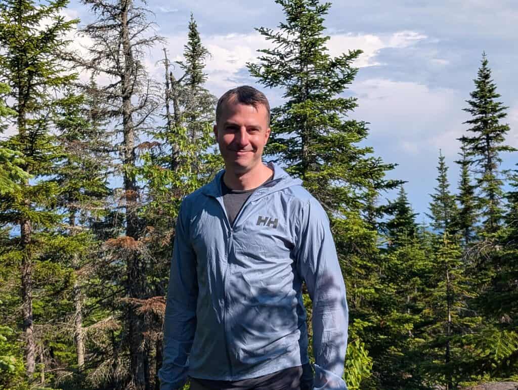 Man in Helly Hansen trail windbreaker jacket hiking in a forested mountain area.