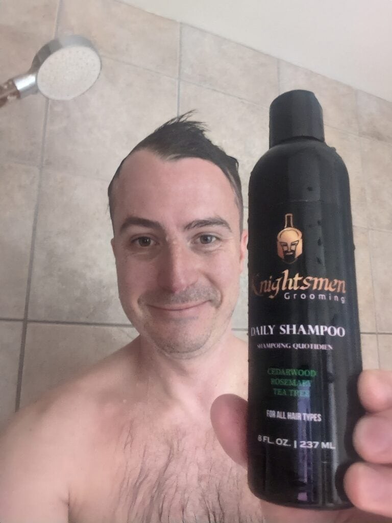 A woman holding a bottle of Nightsmen Grooming Daily Shampoo in a bathroom shower.