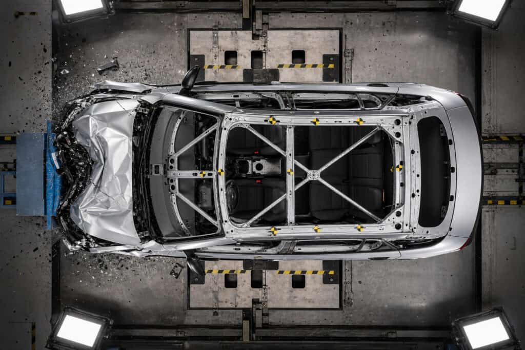 Top-down view of a silver car undergoing crash testing in a controlled environment, with impact sensors and safety equipment visible.