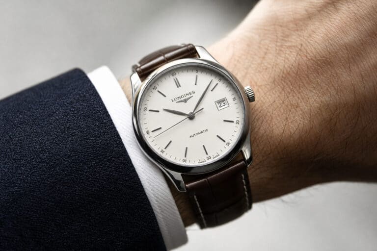 Close-up of a sophisticated Longines automatic wristwatch with a white dial, date display, and brown leather strap on a man's wrist.