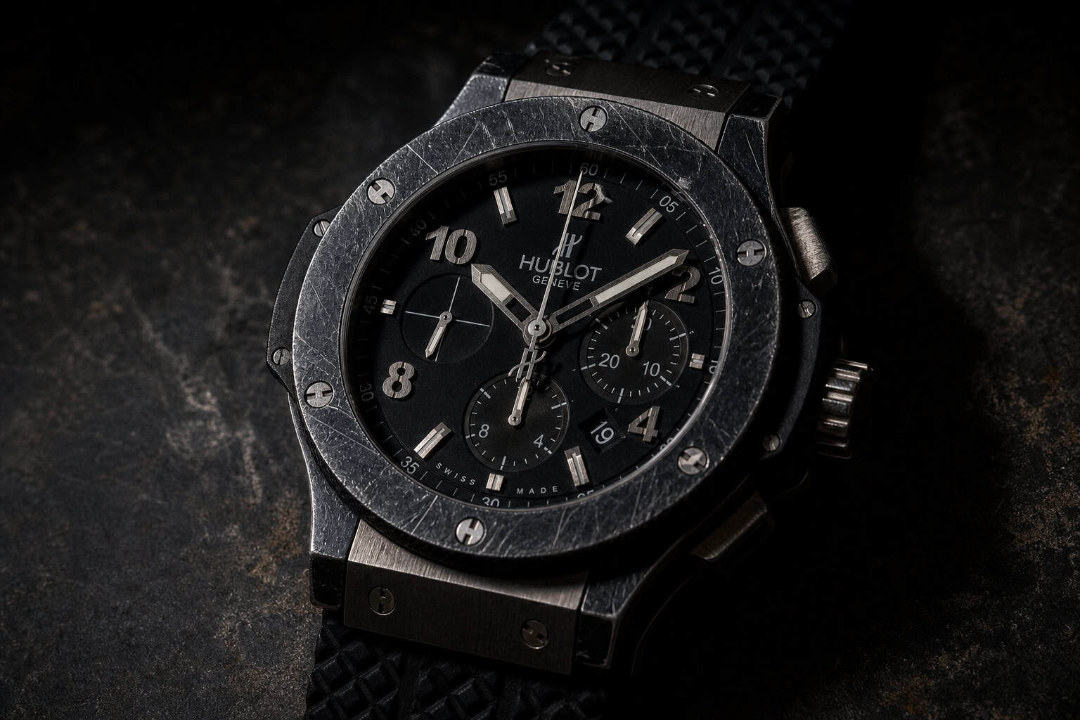 Worn Hublot Big Bang watch on dark surface, dramatic lighting showing scratches and depreciation.