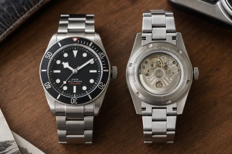Two luxury stainless steel dive watches on a wooden surface, one showing the watch face and the other displaying the transparent back with visible movement.