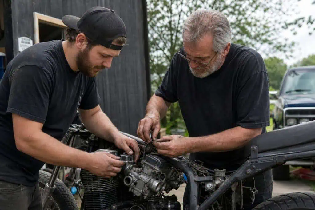 How to Be a Man: Why Kindness, Not Toughness, Is the Metric of Maturity 10 Father and son repairing a motorcycle engine outdoors, focusing on mechanical work and maintenance.