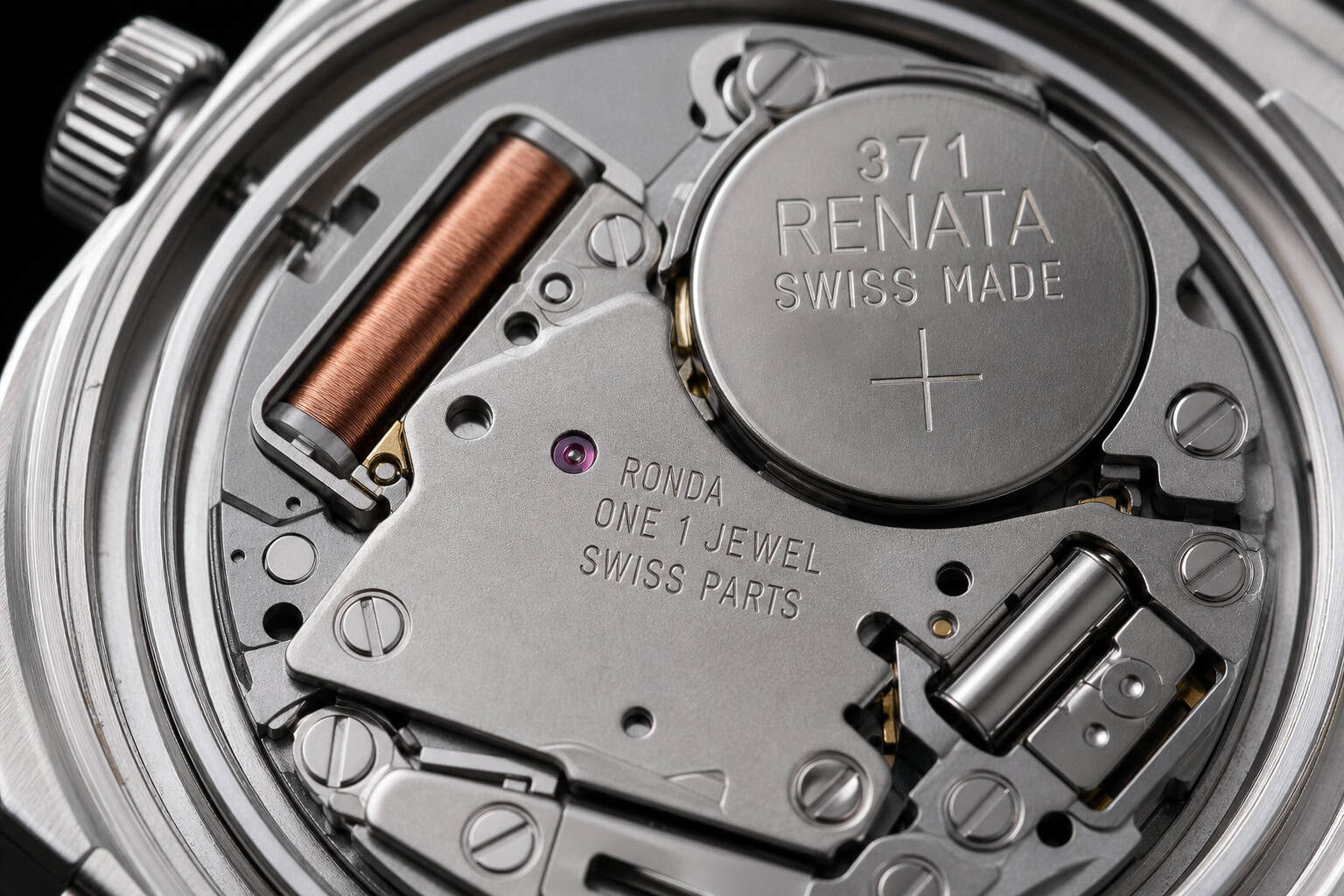 Macro photograph of quartz watch movement with visible battery and metal components.