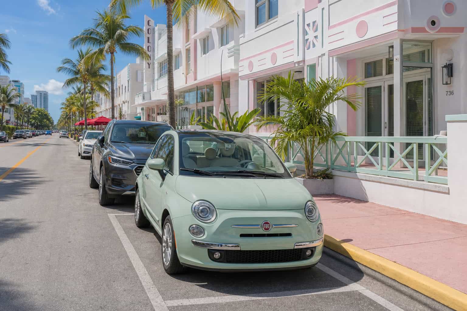 Compact car parked in a tight street parking spot in South Beach with palm trees.