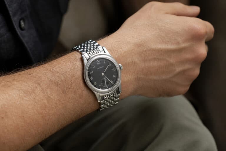 Close-up of a men's silver wristwatch with a black dial, worn on a person's wrist, showcasing elegant and timeless watch design.