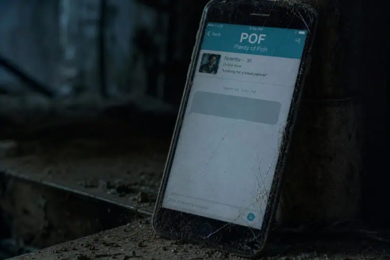 A cracked smartphone displaying a messaging app called POF, lying on a railway track in a dark, outdoor setting.