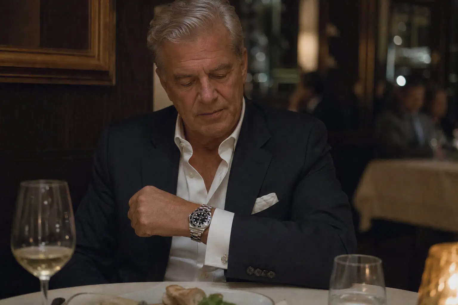 Omega vs Rolex Owners: Age, Income, and What Drives the Choice 5 Older man wearing a Rolex Submariner watch at a dinner table with soft lighting