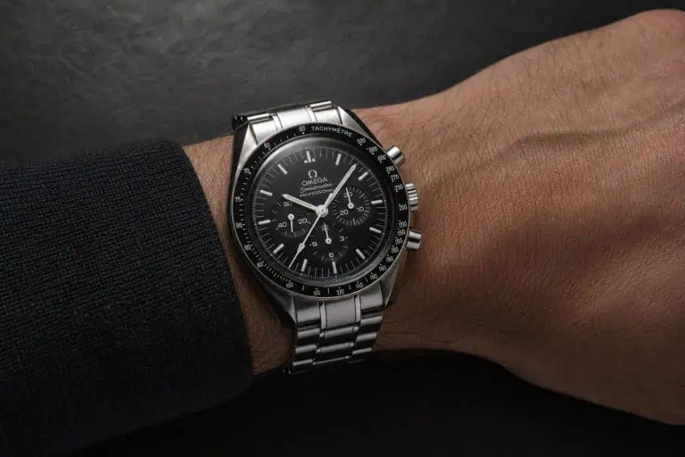 Close-up of Omega Speedmaster Professional chronograph watch on a man's wrist, showcasing its black dial, stainless steel bracelet, and tachymeter bezel.