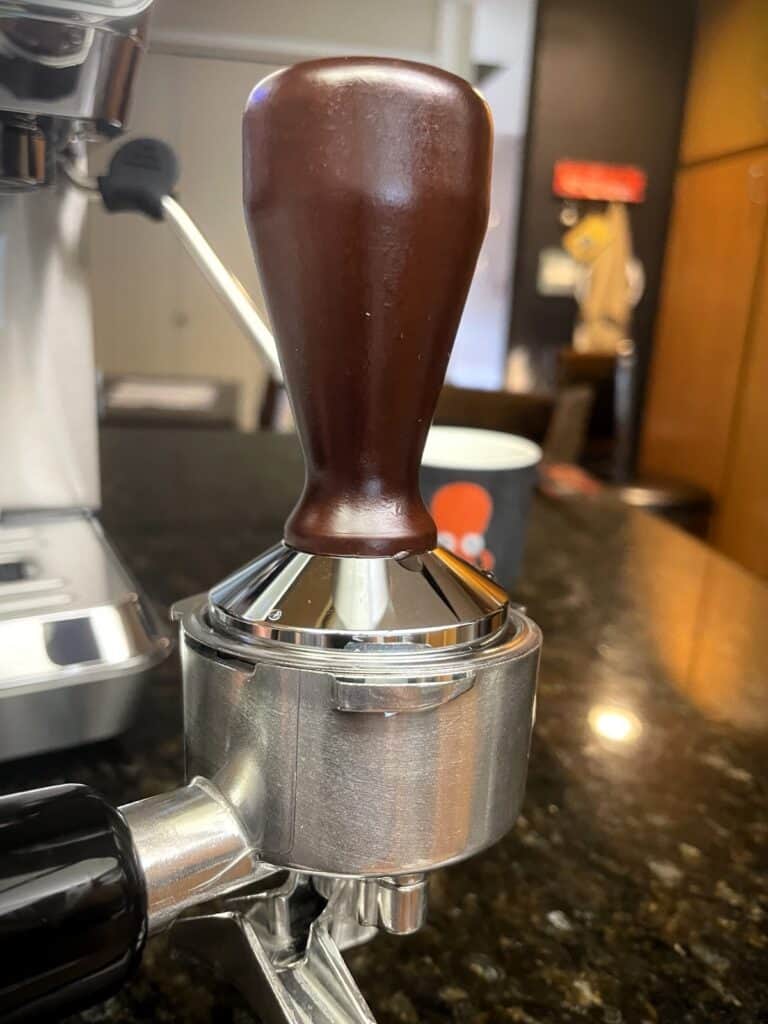 AMZCHEF Espresso Machine Review: 44 Grind Settings and Temperature Control Tested 4 Close-up of a coffee tamper with a wooden handle on a coffee machine portafilter.
