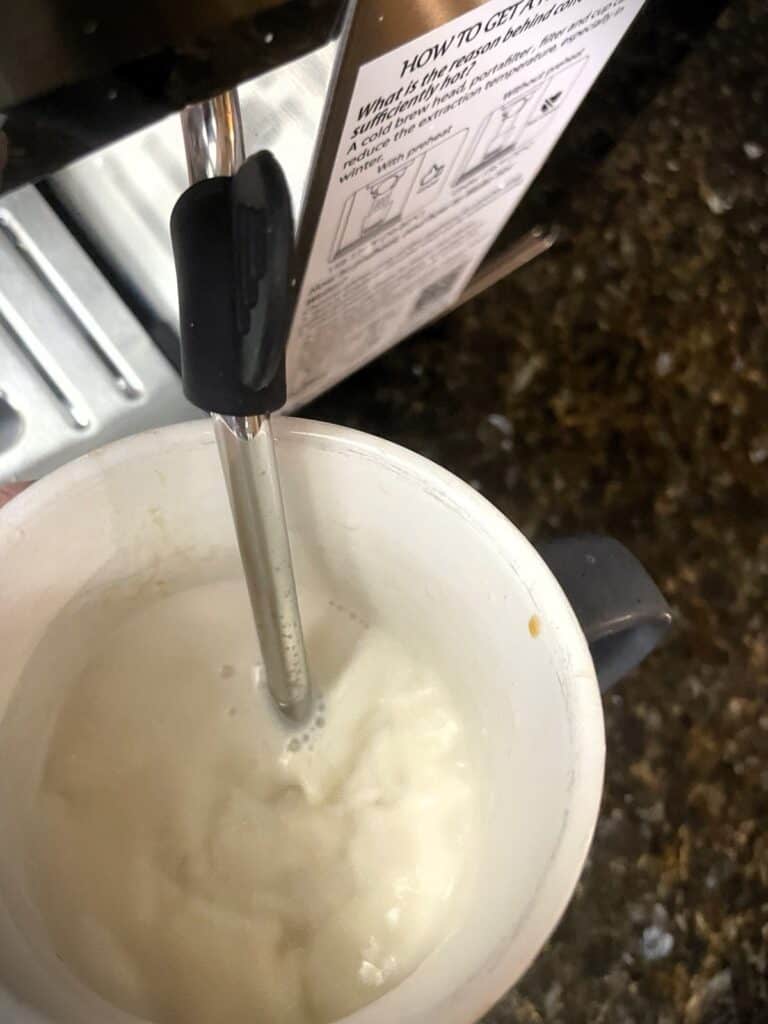 AMZCHEF Espresso Machine Review: 44 Grind Settings and Temperature Control Tested 6 Close-up of an espresso machine frothing milk in a white cup, with a steam wand and instruction label visible.