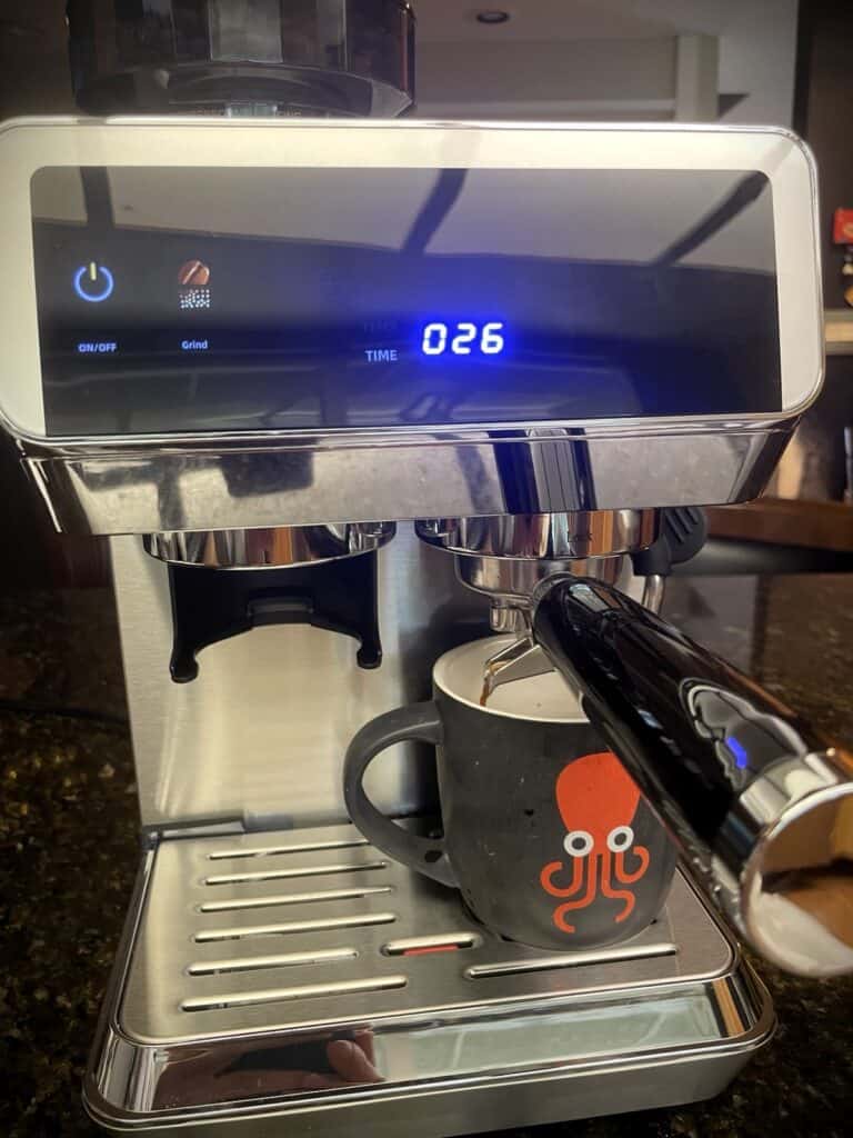 AMZCHEF Espresso Machine Review: 44 Grind Settings and Temperature Control Tested 8 Close-up of an espresso machine brewing coffee into a black mug with a red logo, digital display showing 026 seconds, and a steam wand on a kitchen countertop.