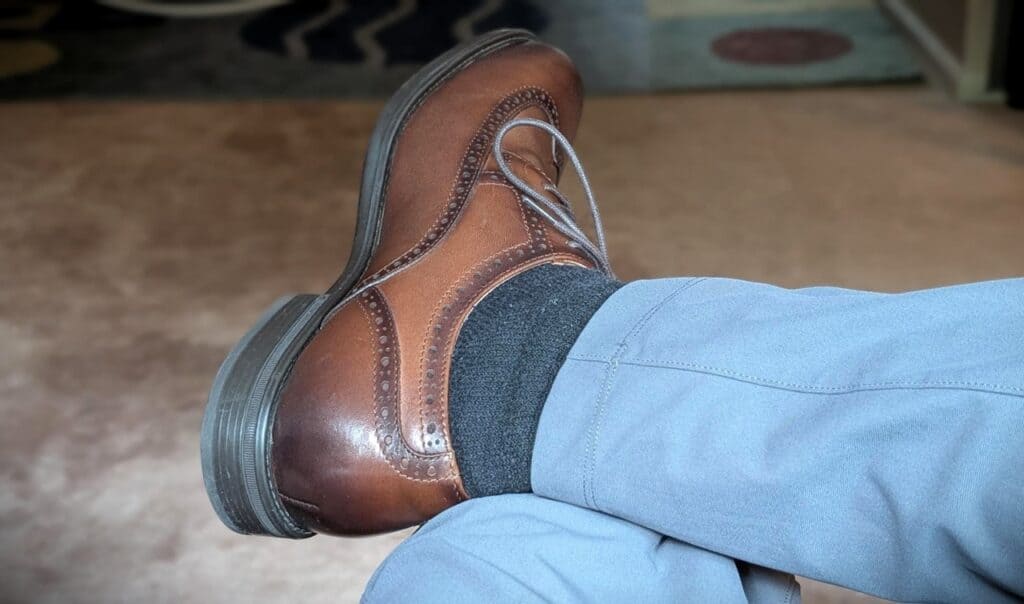 Close-up of a men's brown brogue wingtip oxford shoe worn with blue pants and dark socks, showcasing detailed leather craftsmanship.
